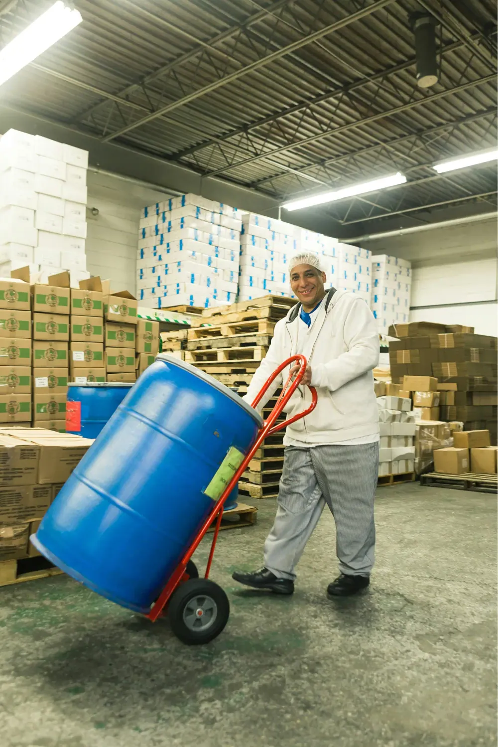 A warehouse worker moving a barrel on a hand truck