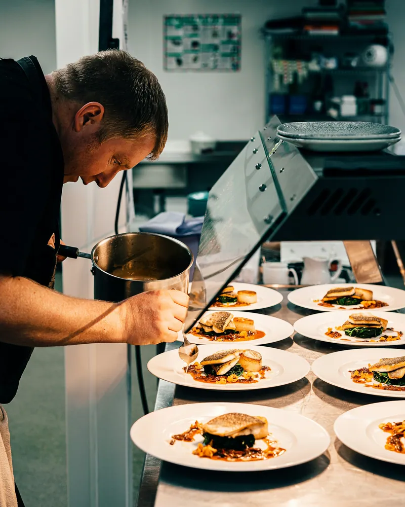 A chef plating up a row of dishes in a commercial kitchen