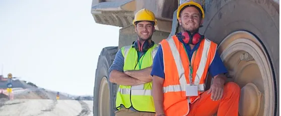 Two mine workers in hi-vis beside heavy equipment